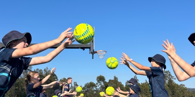 Students throwing and catching netballs during an outdoor sports activity under a clear blue sky