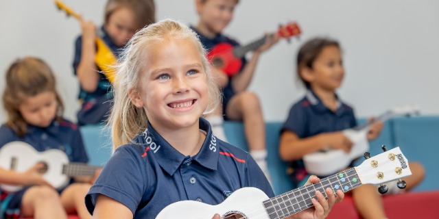 Students playing small ukuleles together during a music class with one student in the foreground